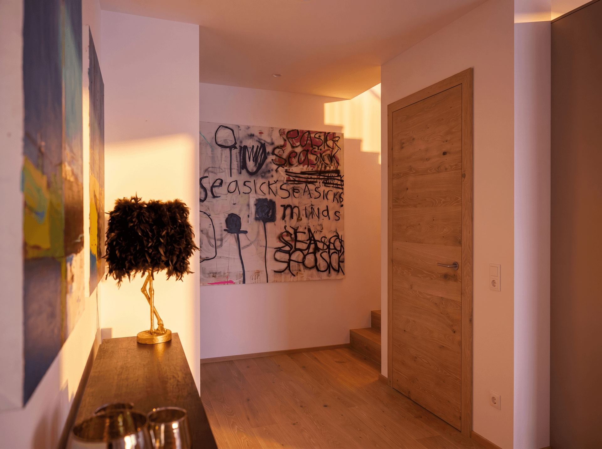 Heller Flur mit Holzboden, einer Konsole und moderner Kunst, der zu weiteren Räumen und einer Treppe führt.