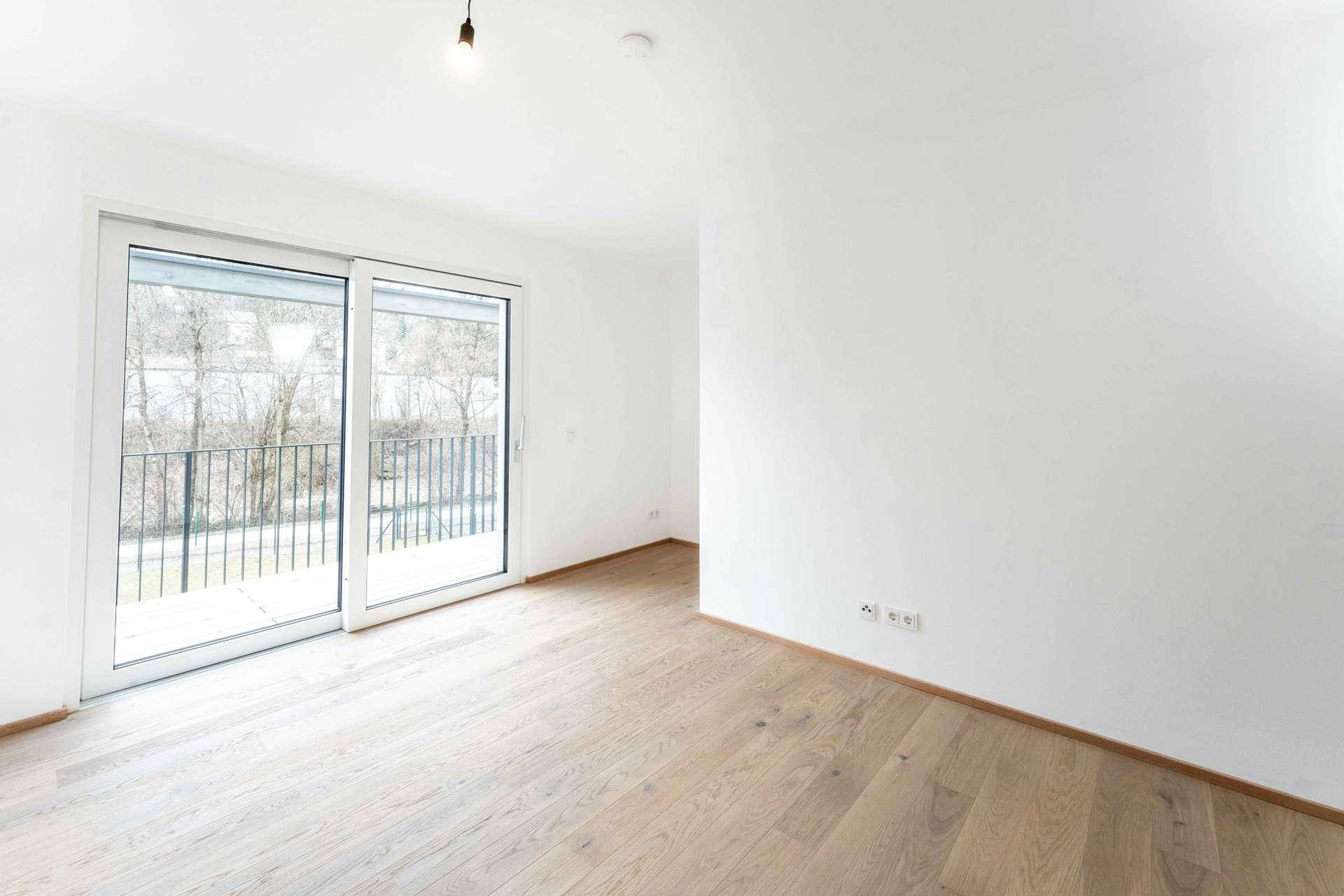 Helles, leeres Zimmer mit Holzboden und Zugang zu einem Balkon, bereit zum Einrichten.