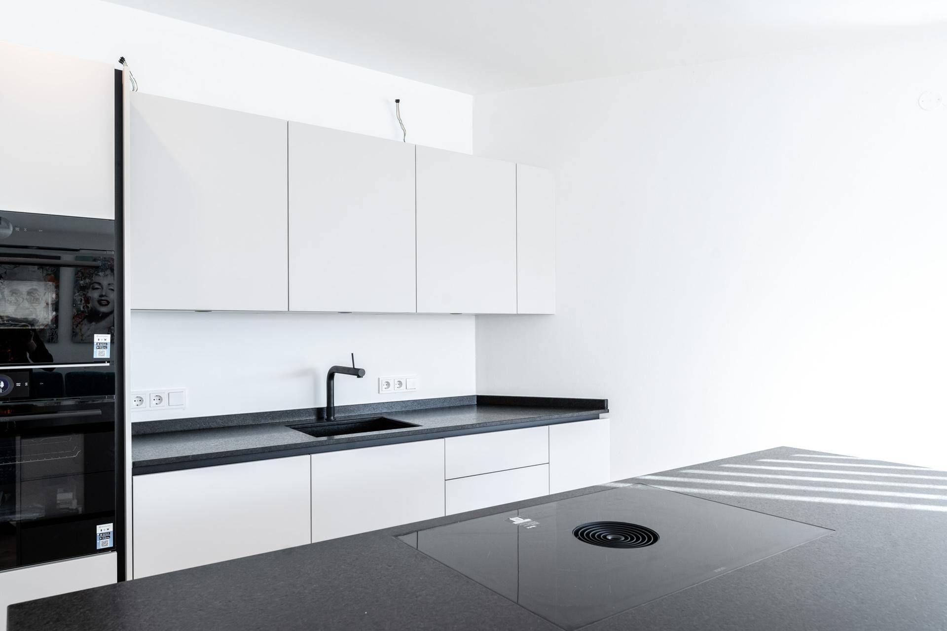 Moderne weiße Küche mit schwarzen Arbeitsplatten, integrierten Geräten und Induktionskochfeld.