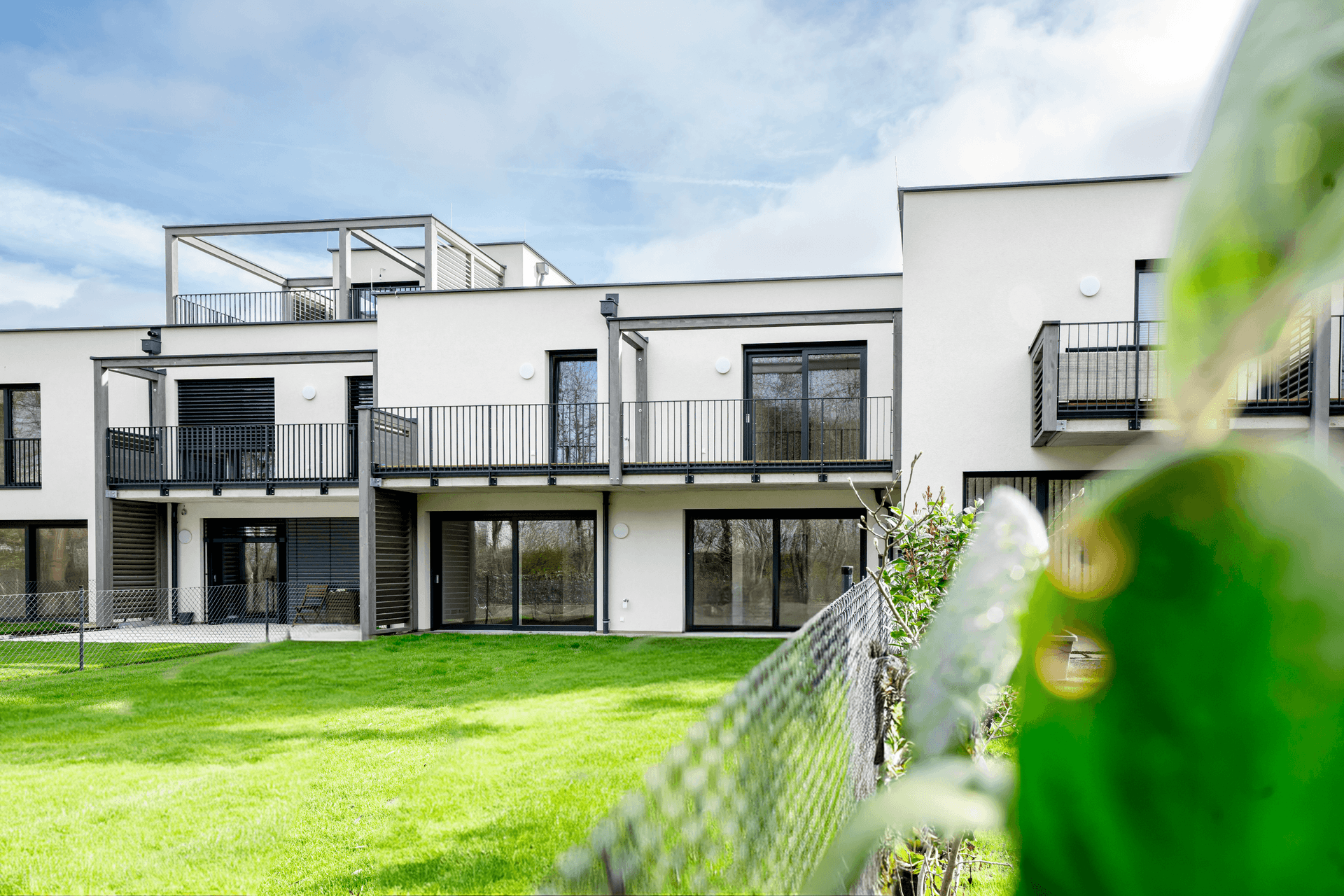 Moderne Wohnanlage mit weißer Fassade, Balkonen, Terrassen und gepflegtem Rasenbereich.
