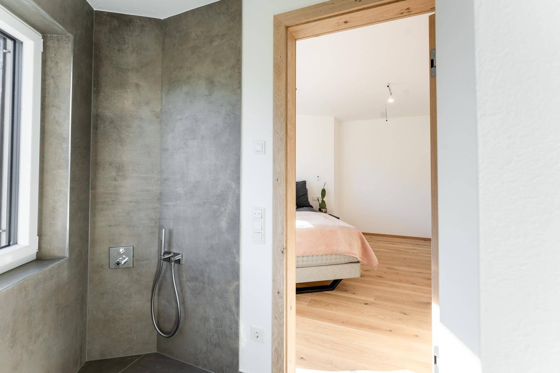 Modernes Badezimmer mit begehbarer Dusche und Fenster, mit Blick ins angrenzende Schlafzimmer.