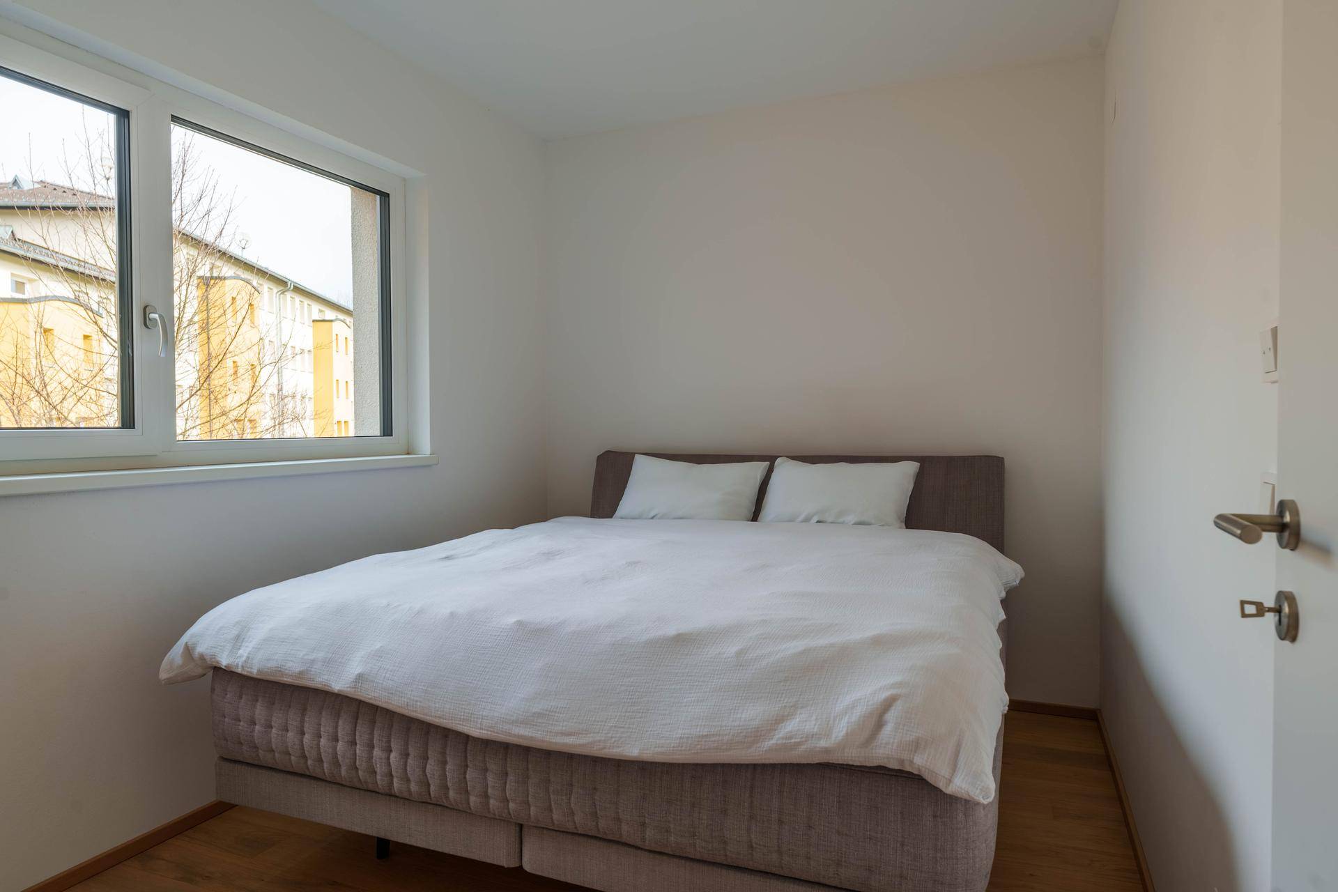 Helles Schlafzimmer mit Bett und Fenster, das einen Blick auf die Umgebung bietet.