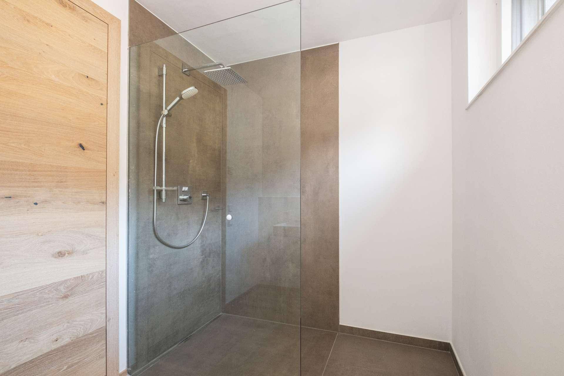 Geräumige, moderne Dusche mit Glasabtrennung und großformatigen grauen Fliesen.