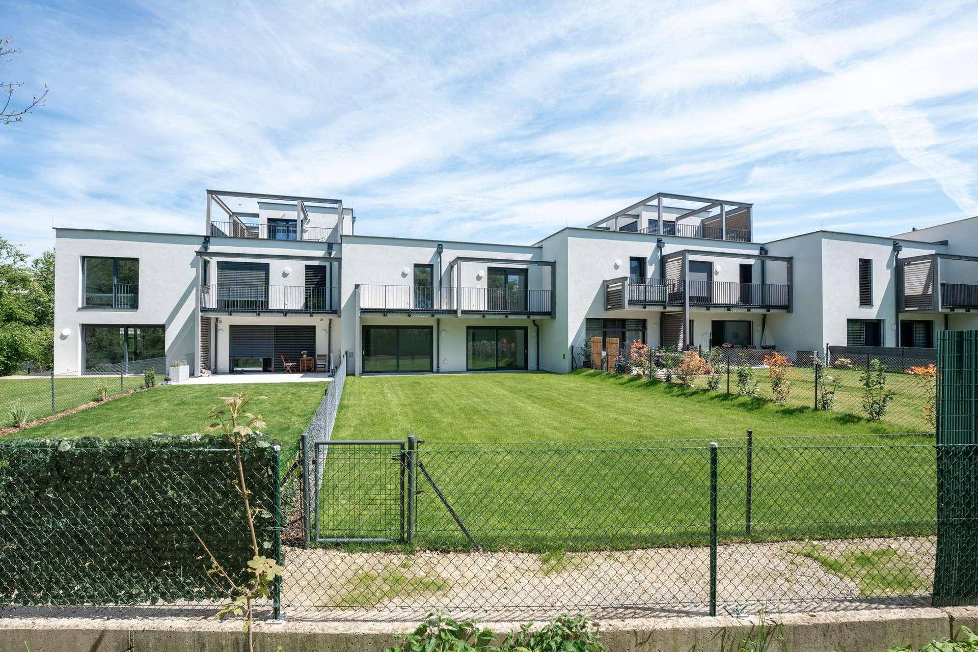 Neubau-Reihenhäuser mit großzügigen Gärten und sonnigen Balkonen unter blauem Himmel.