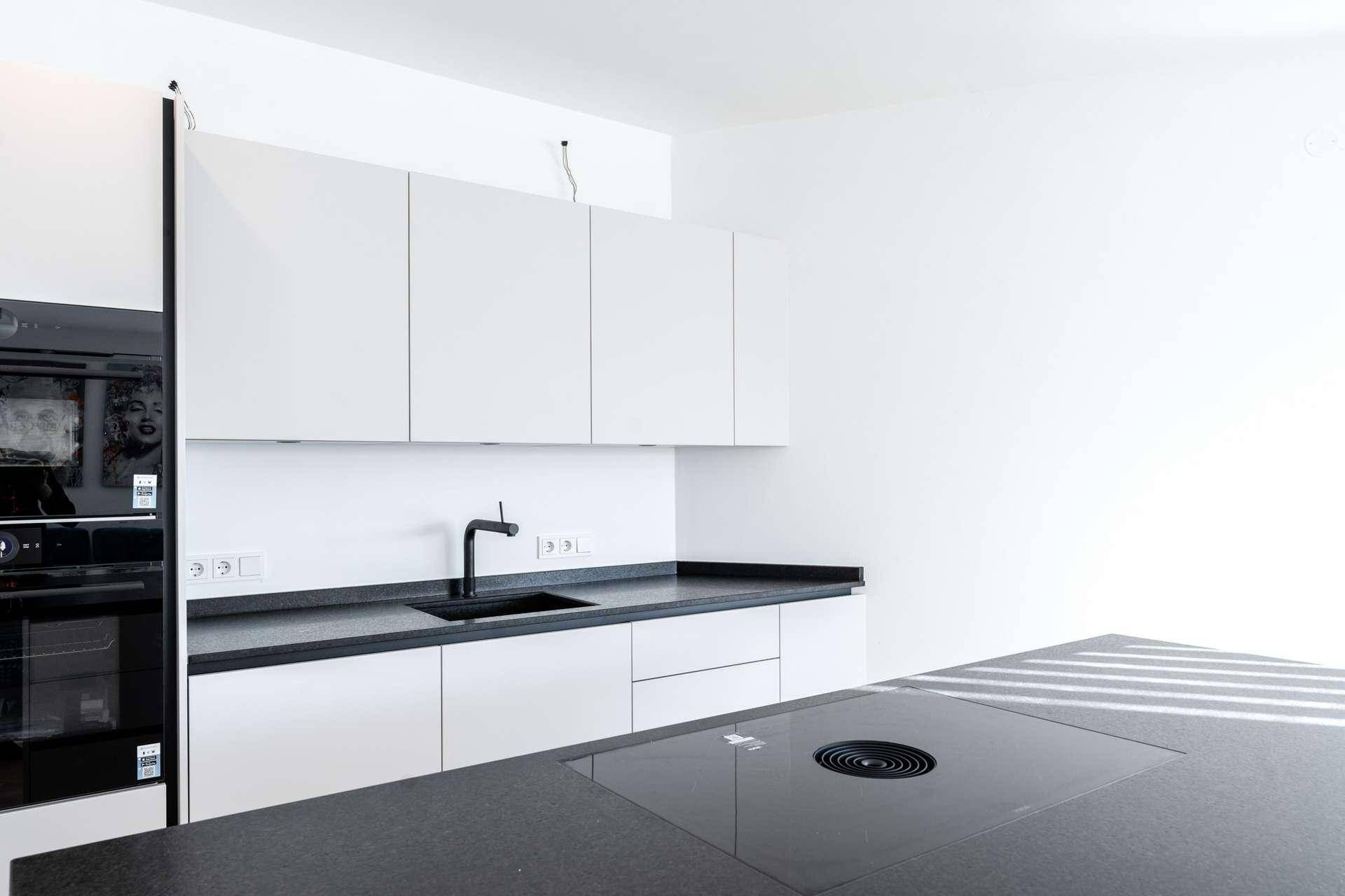 Moderne Küche mit weißen Schränken, dunklen Arbeitsplatten und integriertem Induktionskochfeld.