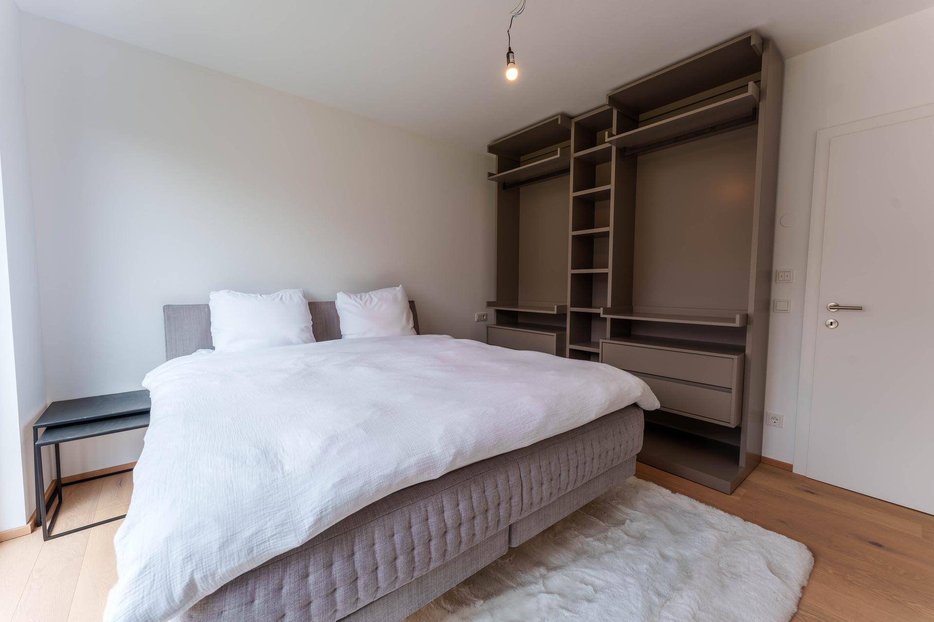Schlafzimmer mit Doppelbett, offenem Kleiderschrank und hellem Holzboden.