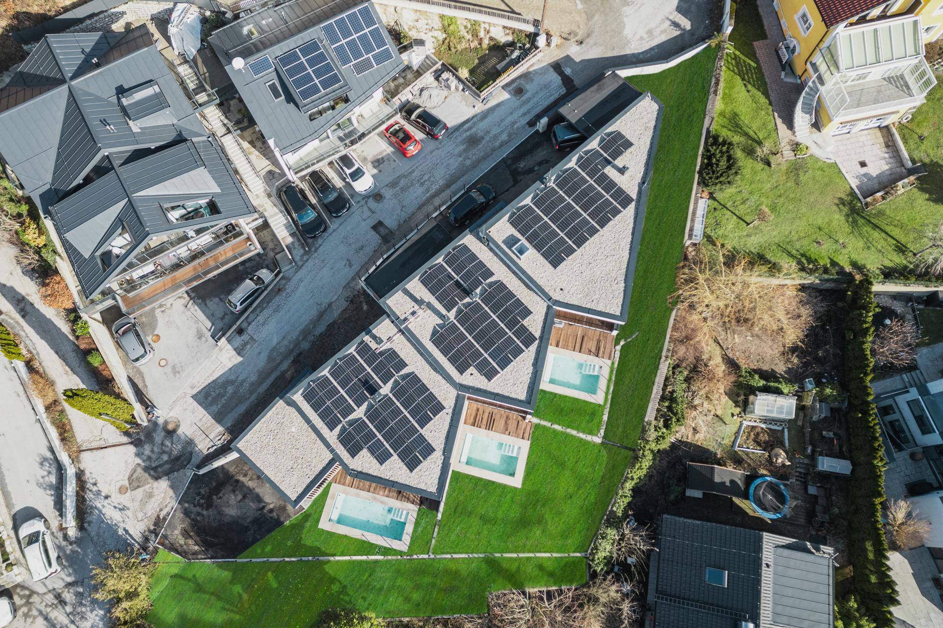Draufsicht auf die moderne Wohnanlage mit Flachdächern, Photovoltaikanlagen und Pools.