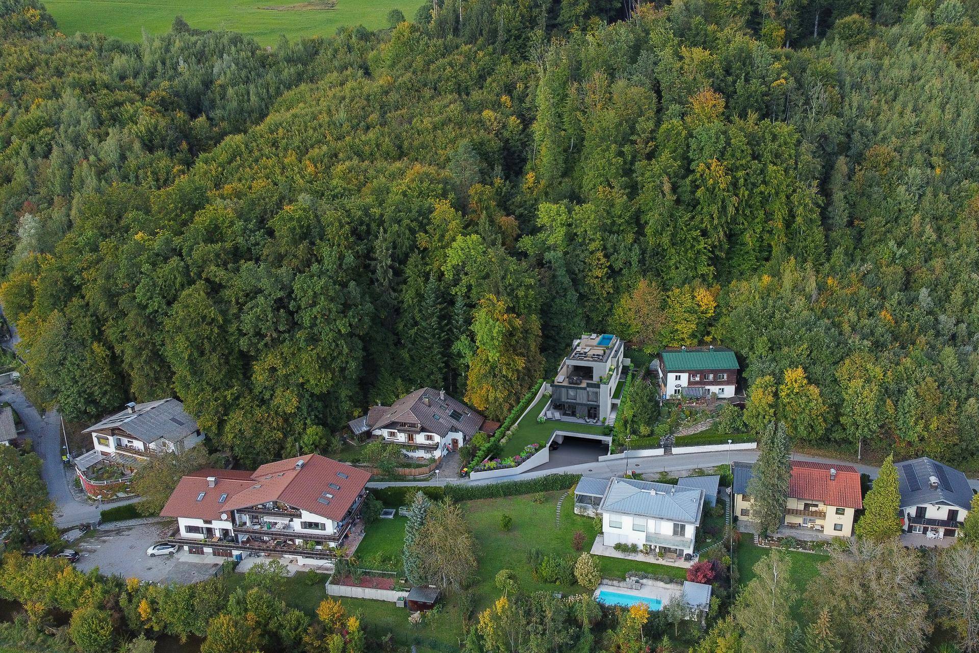 Luftaufnahme der modernen Villa in einer grünen Wohngegend mit umliegenden Häusern und Wald.