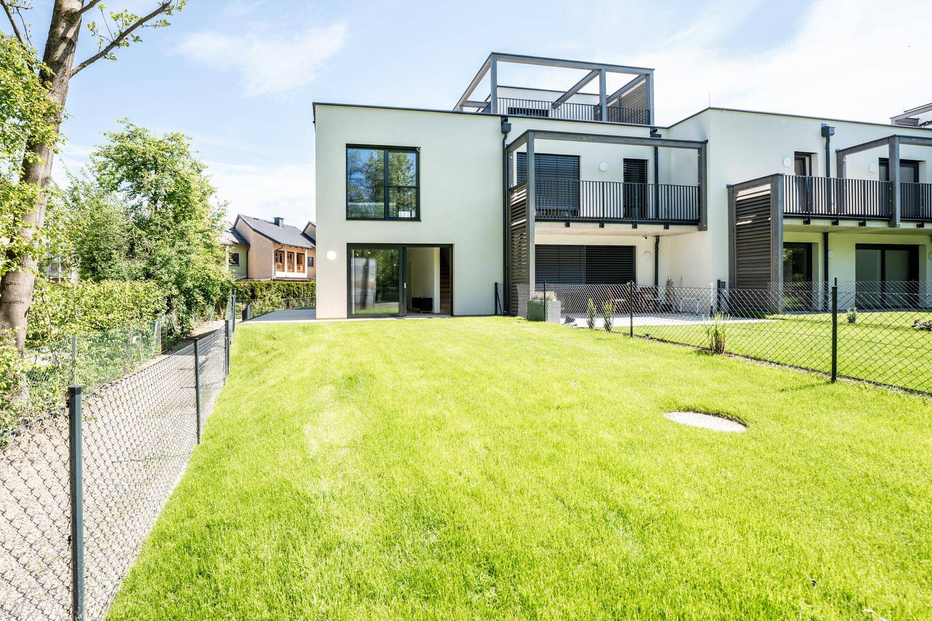 Modernes Mehrfamilienhaus mit weißer Fassade, Balkonen und großem, gepflegtem Rasenbereich.