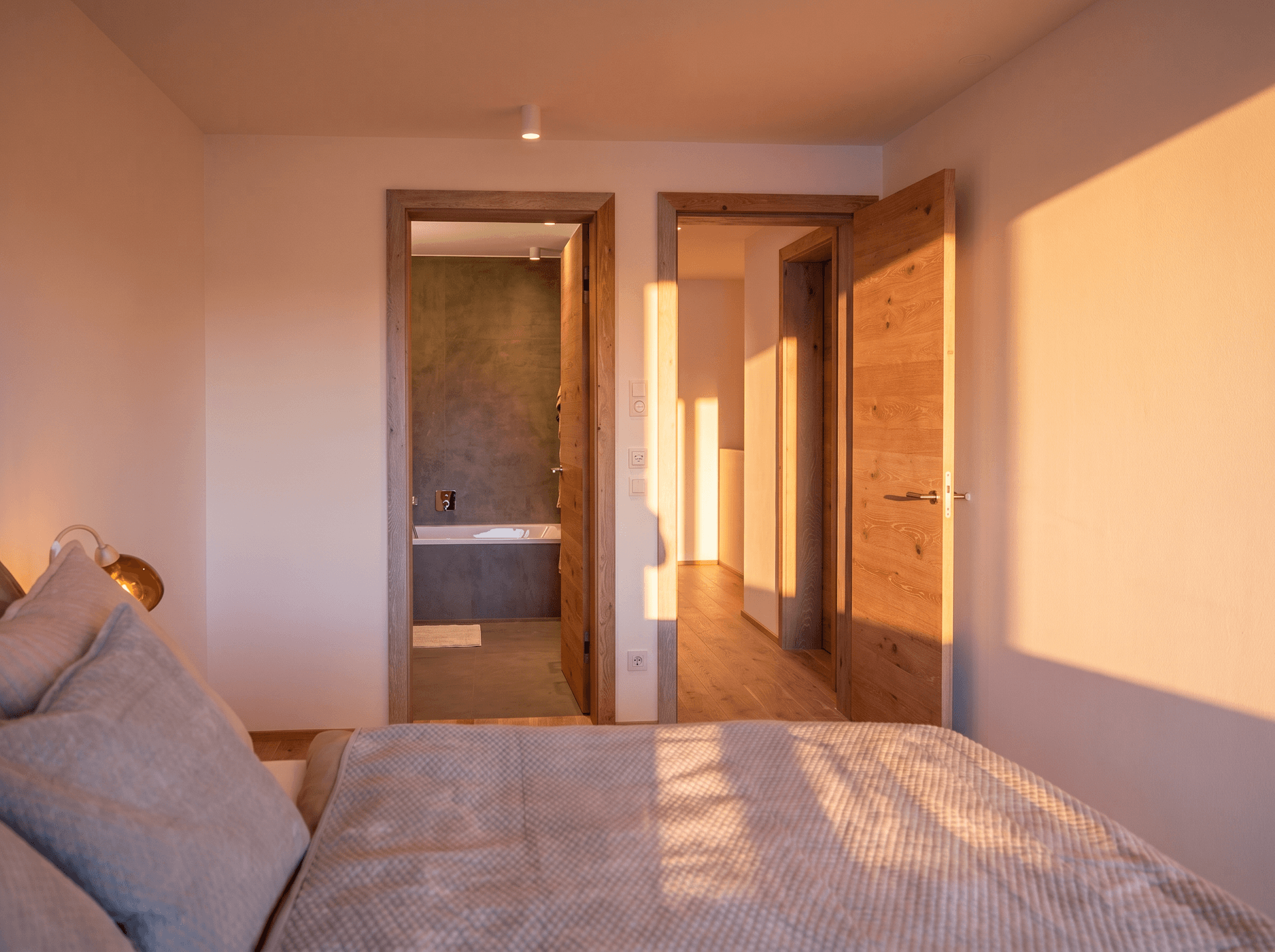 Schlafzimmer mit Blick auf zwei Holztüren, eine führt zu einem Badezimmer mit Badewanne, die andere zu einem weiteren Raum.