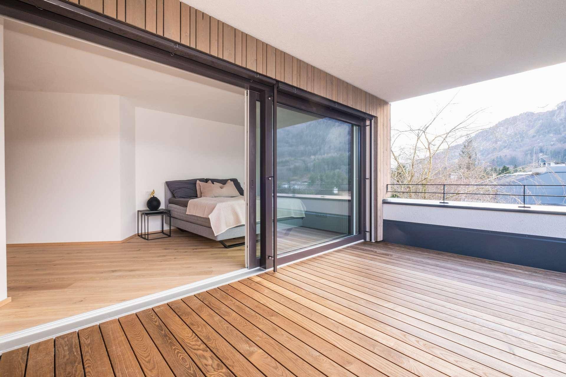 Helles Schlafzimmer mit Holzboden und großem Schiebefenster zum Balkon mit Bergblick.