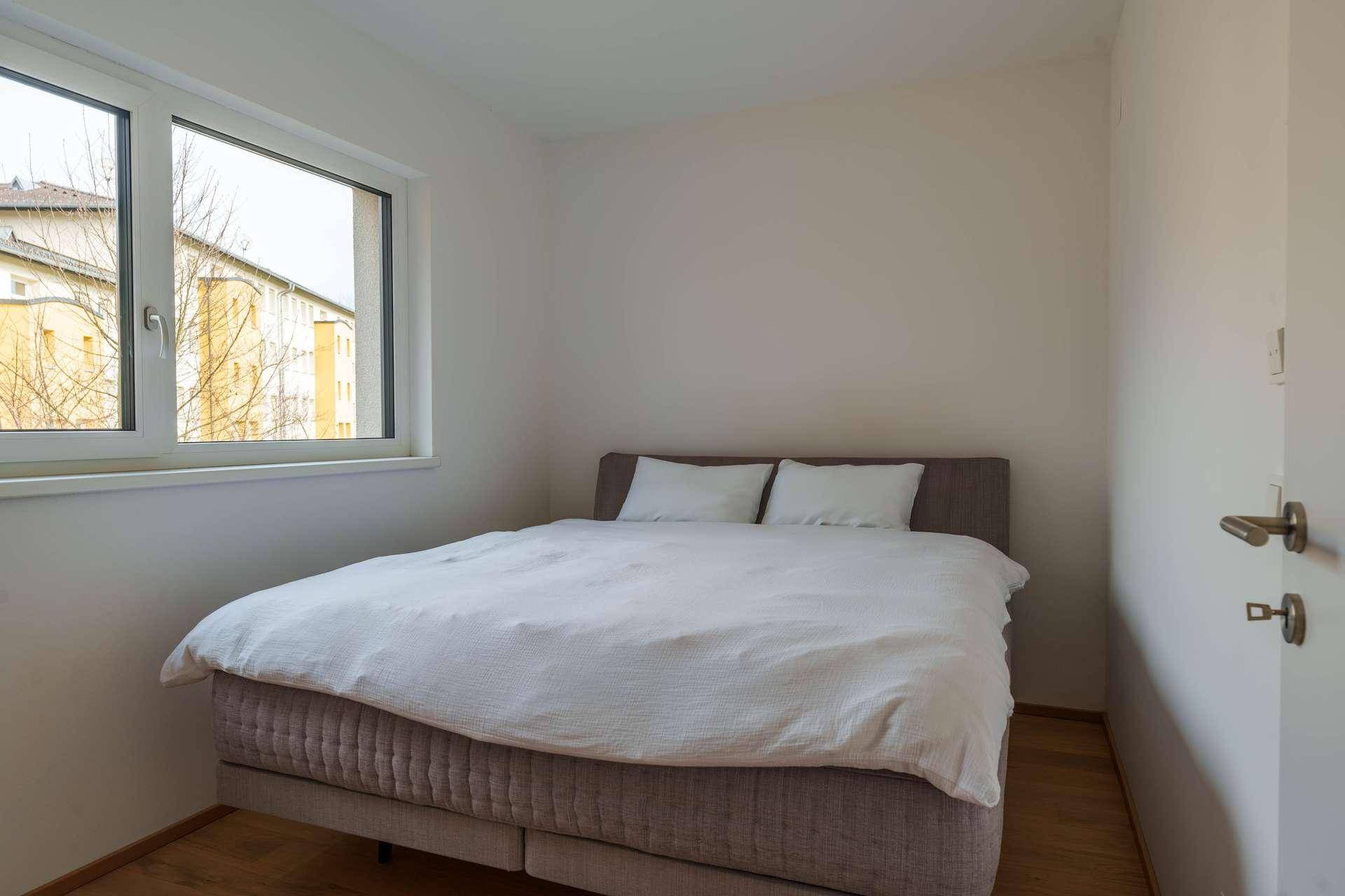 Gemütliches Schlafzimmer mit Doppelbett und Fenster, das Tageslicht hereinlässt.