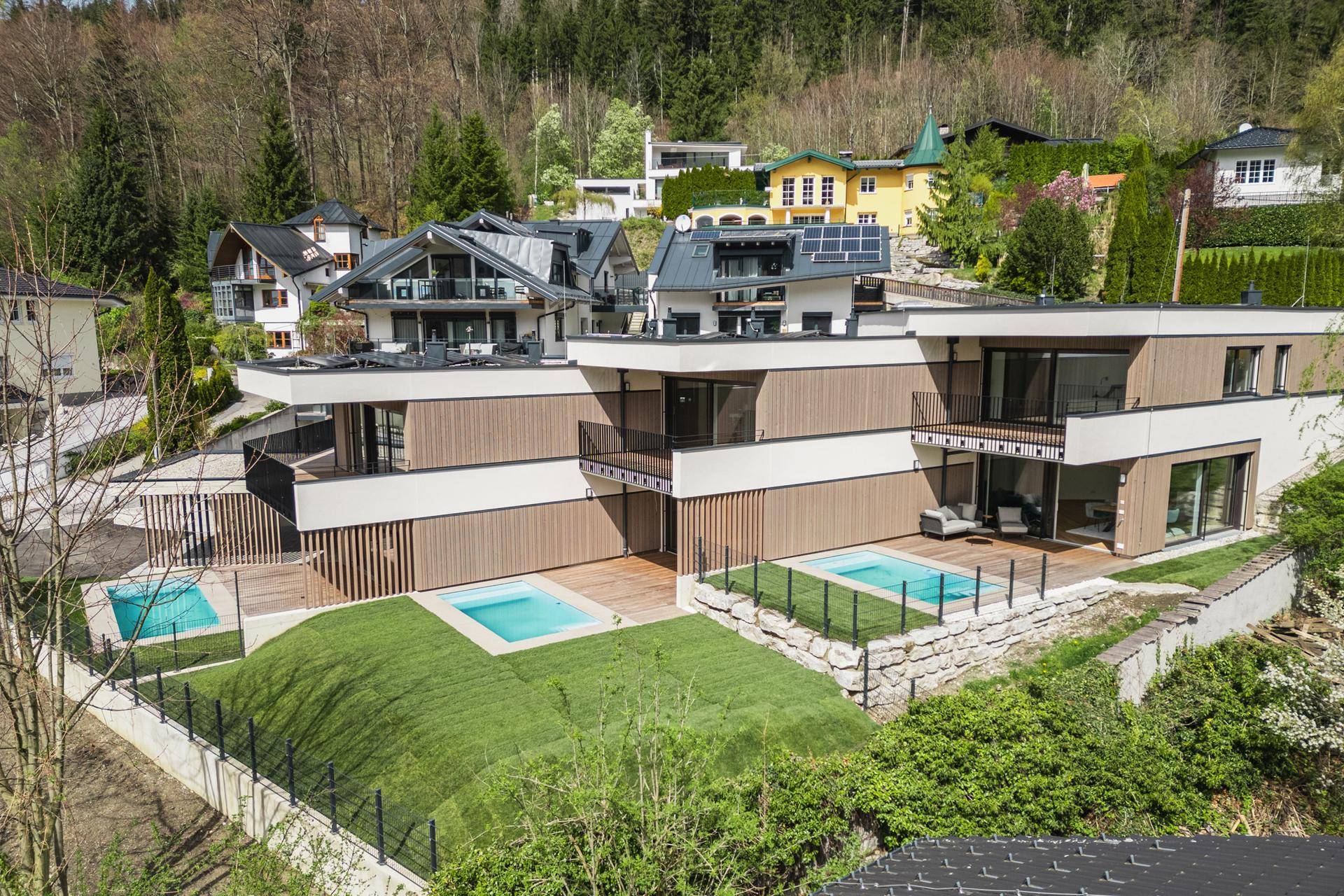 Panoramablick auf die moderne Wohnanlage mit Pools, Photovoltaikanlagen und umliegender Natur.