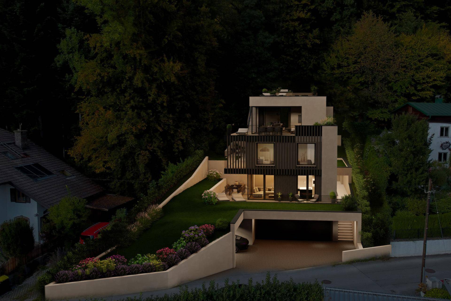 Moderne Villa bei Nacht, beleuchtet und eingebettet in die bewaldete Hanglandschaft.