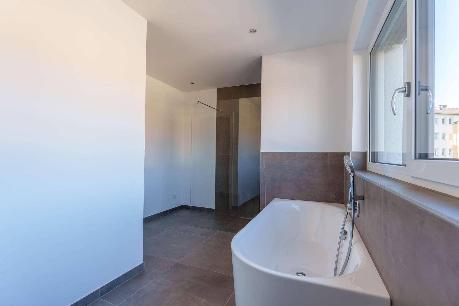 Modernes Badezimmer mit Badewanne, begehbarer Dusche und großem Fenster für Tageslicht.