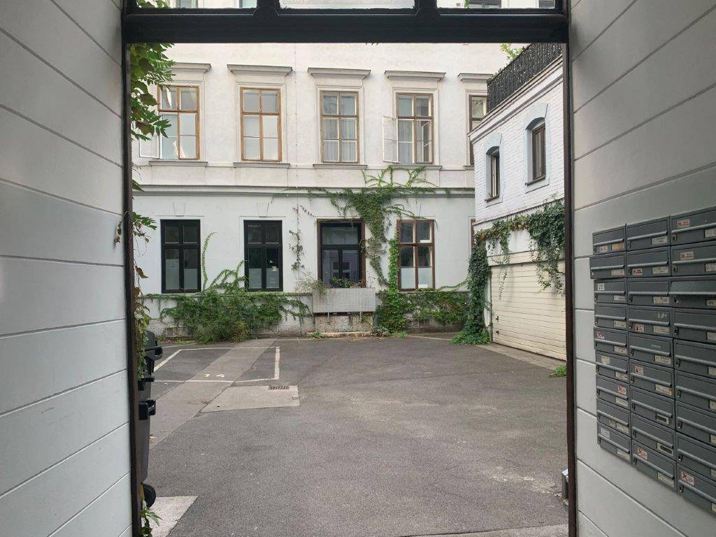 Blick in einen ruhigen Innenhof mit Gebäudefassaden, Fenstern und Briefkästen.