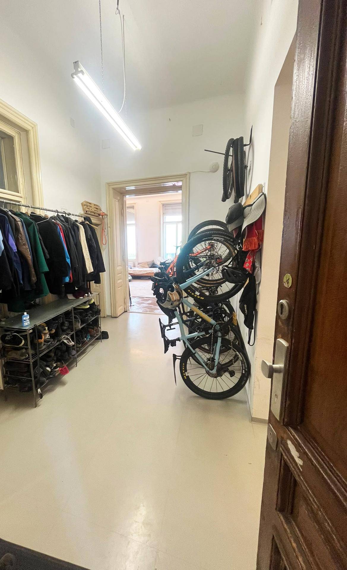 Lagerraum mit Fahrrädern, Kleiderständer und Schuhregal, der zu weiteren Räumen führt.