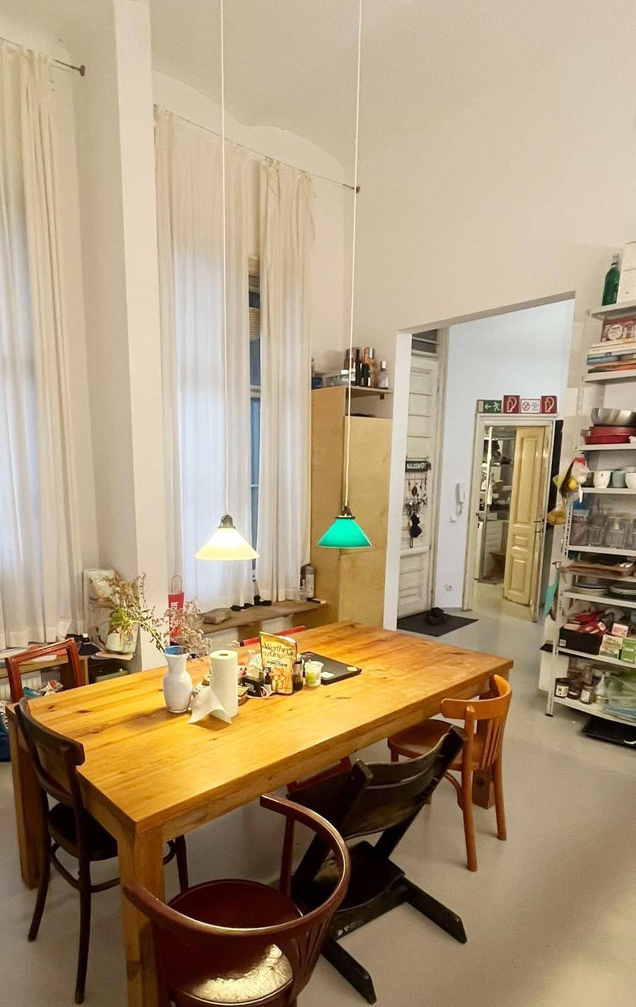 Heller Essbereich mit Holztisch, Stühlen und großen Fenstern mit weißen Vorhängen.