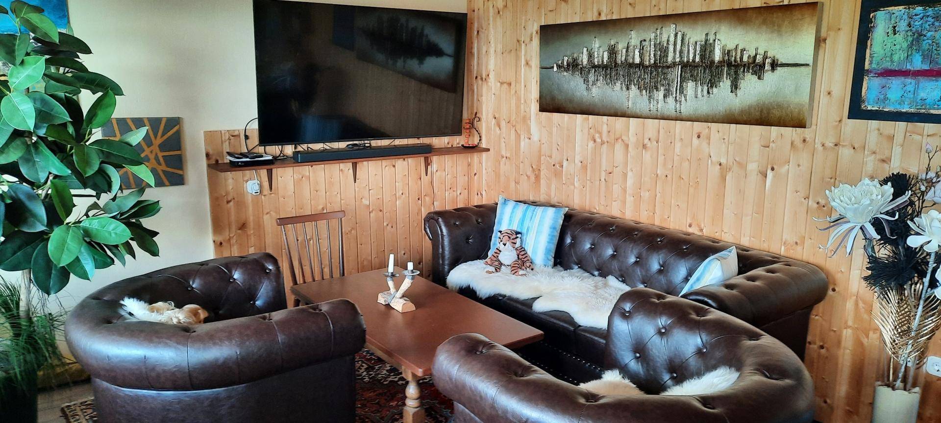 Gemütliches Wohnzimmer im alpinen Stil mit holzvertäfelten Wänden, Ledersofas und einem großen Fernseher.