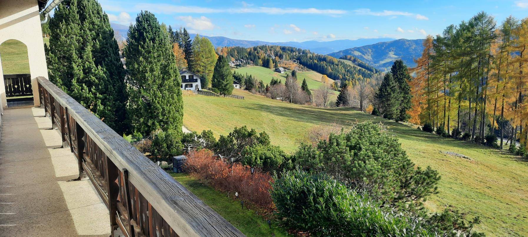 Geräumiger Balkon mit Holzbalkonbrüstung und weitem Blick auf die grüne Berglandschaft.
