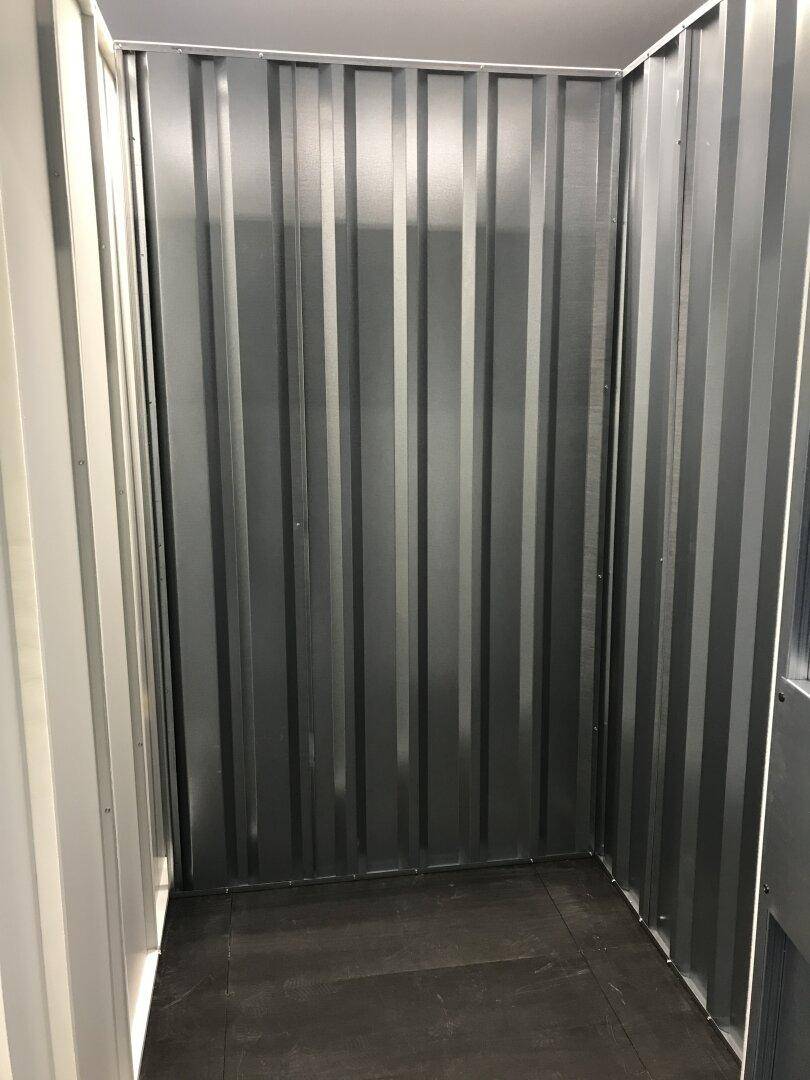 Innenansicht einer einzelnen Lagereinheit mit gewellten Metallwänden und dunklem Boden.