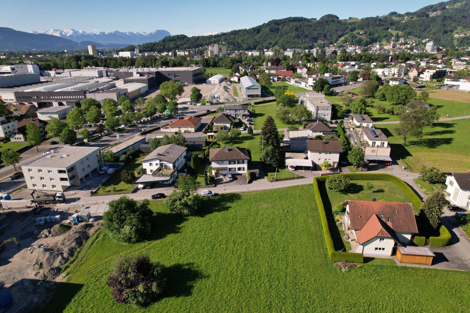Luftaufnahme des Grundstücks mit Blick auf umliegende Bebauung und schneebedeckte Berge am Horizont.