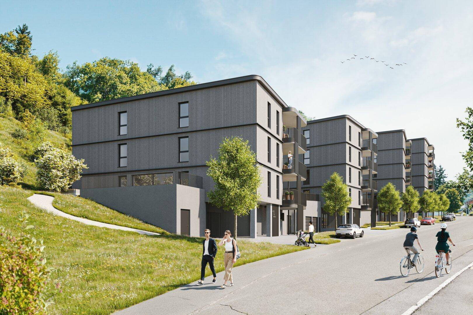 Moderne Wohngebäude mit klarer Architektur entlang einer Straße, eingebettet in eine grüne Hügellandschaft.