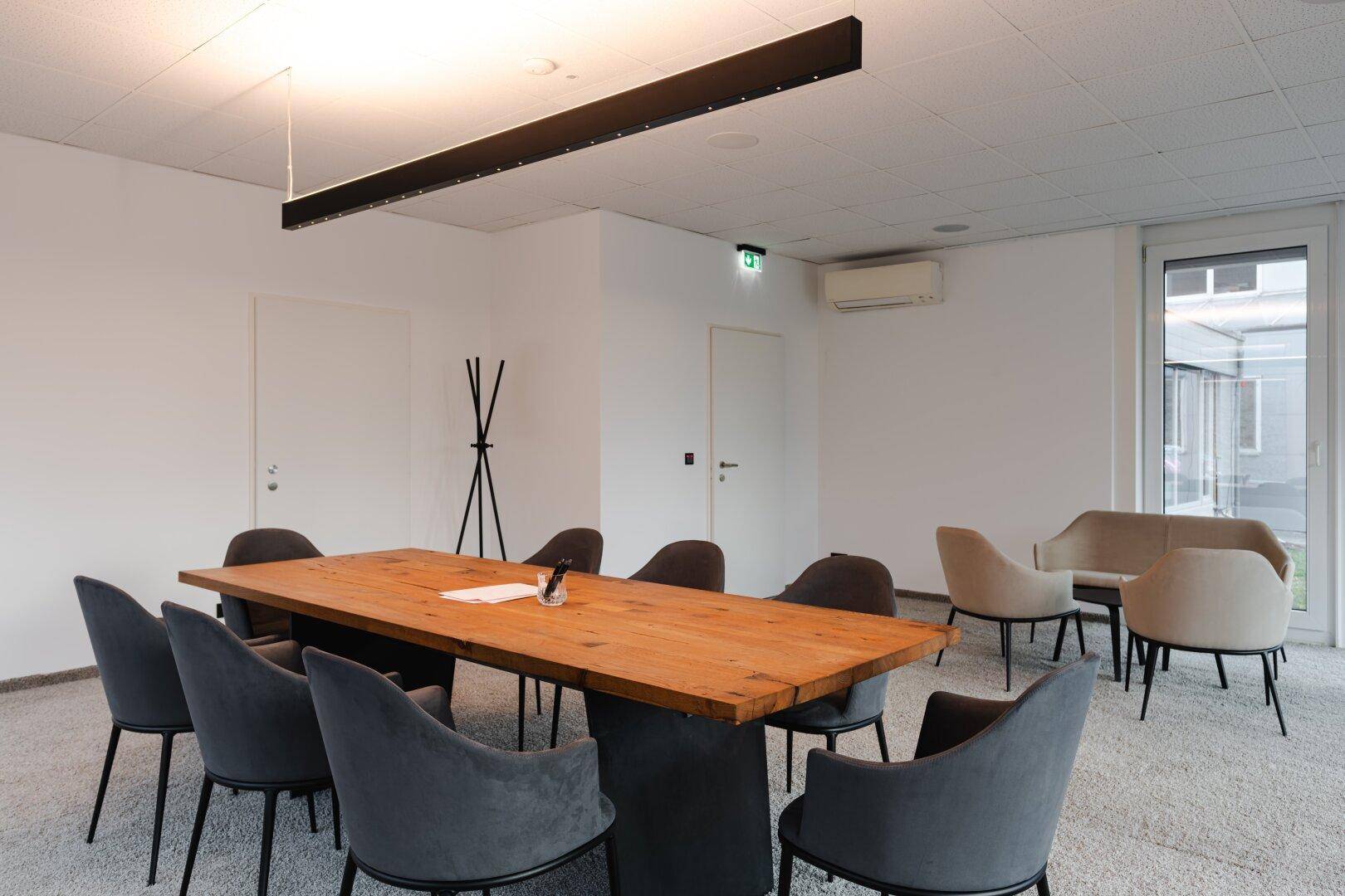 Gemütlicher Besprechungsraum mit Holztisch, bequemen Stühlen und einer kleinen Lounge-Ecke.