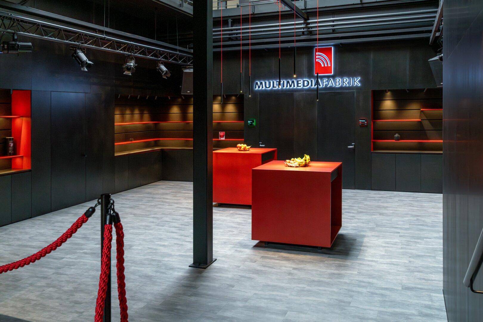 Geräumiger Ausstellungsbereich mit zwei roten Präsentationswürfeln und beleuchteten Wandregalen.