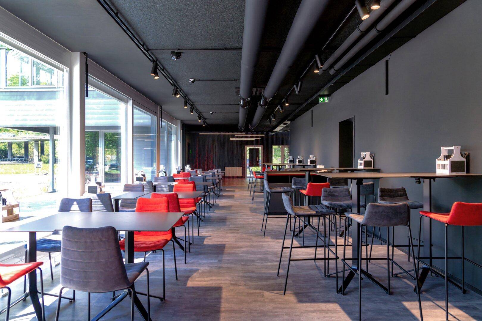 Geräumiger Essbereich mit verschiedenen Sitzgelegenheiten, großen Fenstern und industriellem Decken-Design.