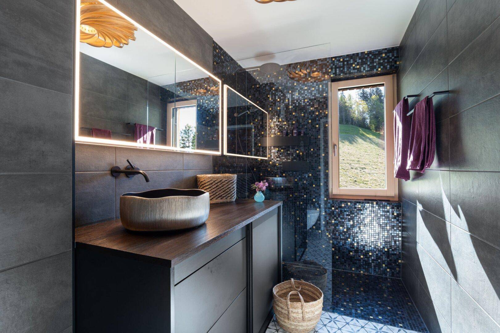 Modernes Badezimmer mit dunklen Fliesen, stilvollem Waschbecken und begehbarer Dusche mit Mosaikfliesen.
