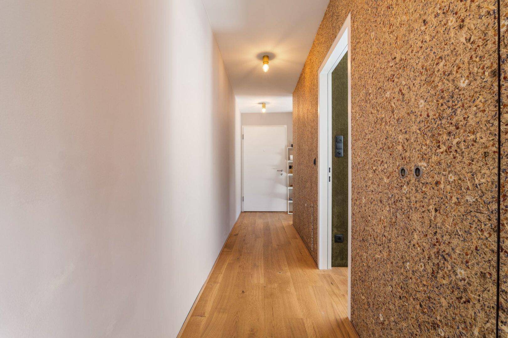 Langer, heller Flur mit Holzboden und einer auffälligen strukturierten Wand.