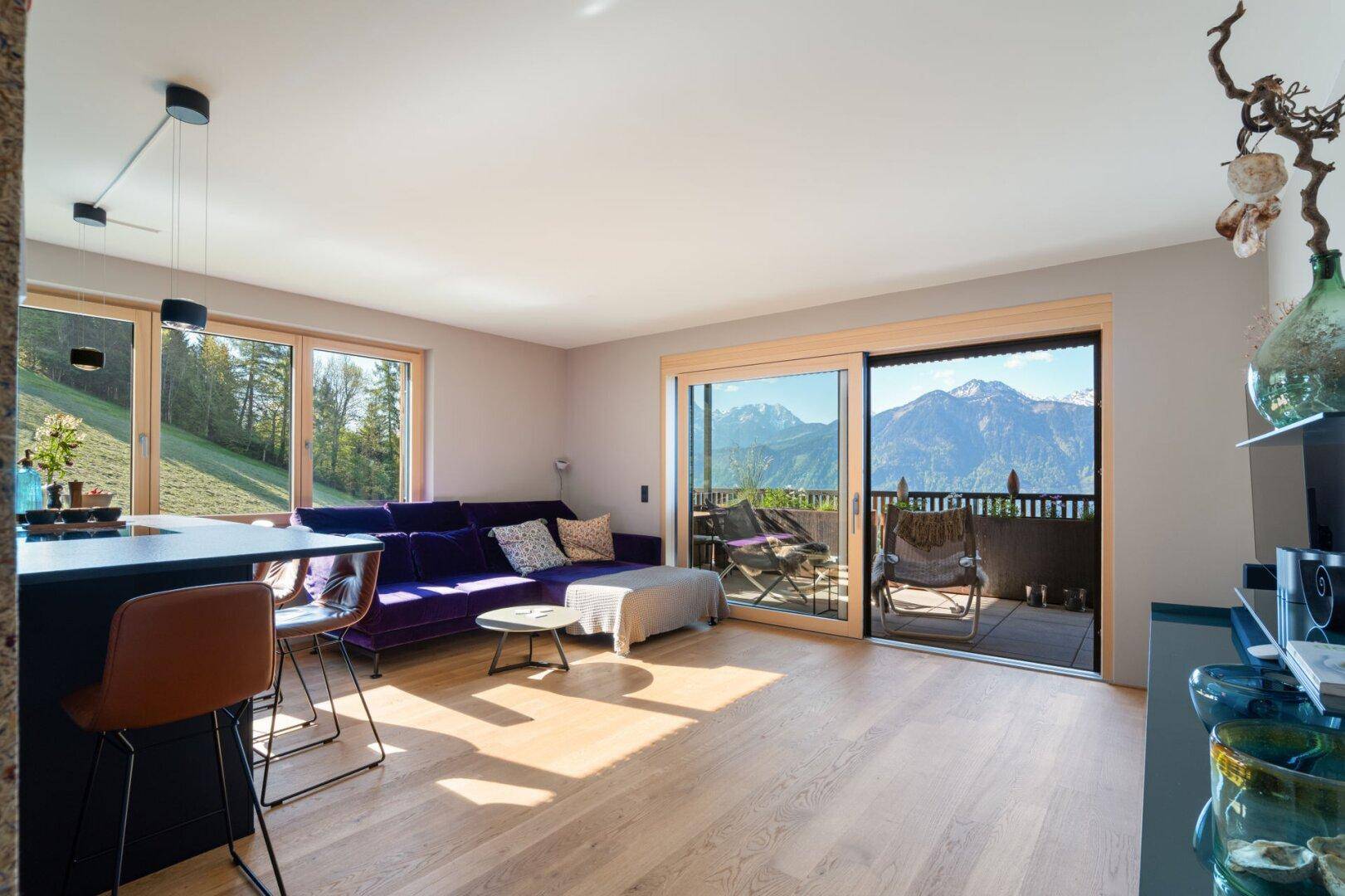 Helles Wohn- und Esszimmer mit offener Küche, Holzboden und Zugang zu einem Balkon mit Bergblick.