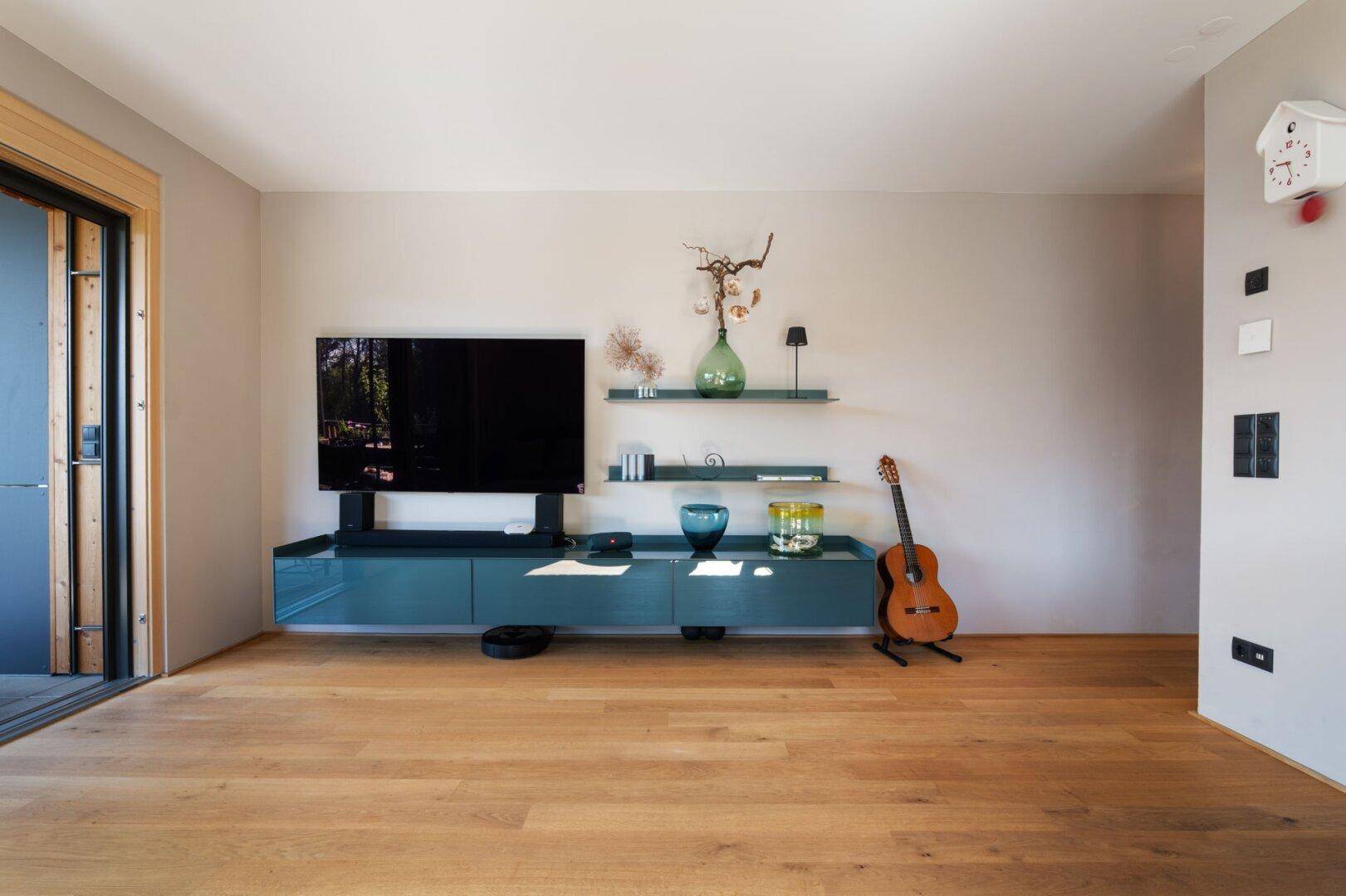 Gemütlicher Wohnbereich mit modernem TV-Möbel, Holzboden und Zugang zur Terrasse oder Balkon.