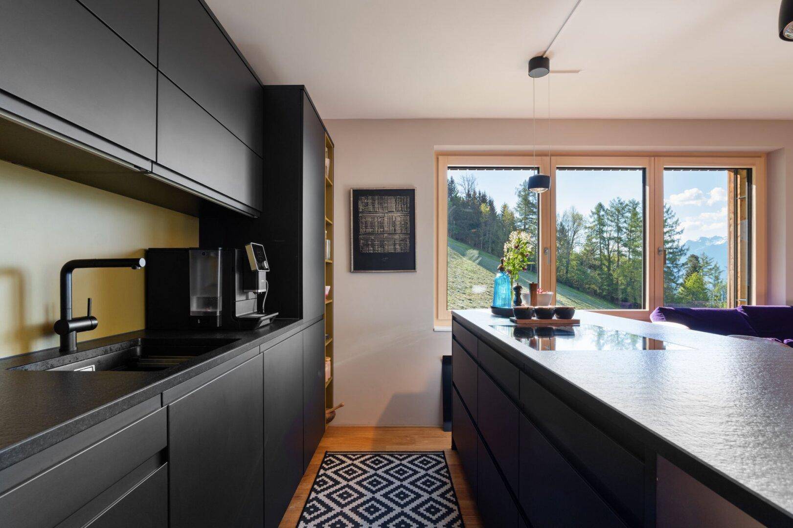 Moderne schwarze Küche mit integrierten Geräten, Spüle und Fenster mit Blick auf die grüne Landschaft.