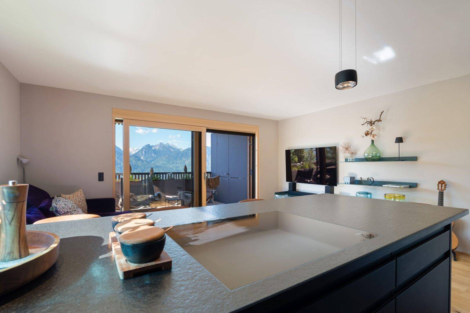 Offener Wohnbereich mit Kücheninsel und direktem Zugang zum Balkon mit atemberaubendem Bergblick.