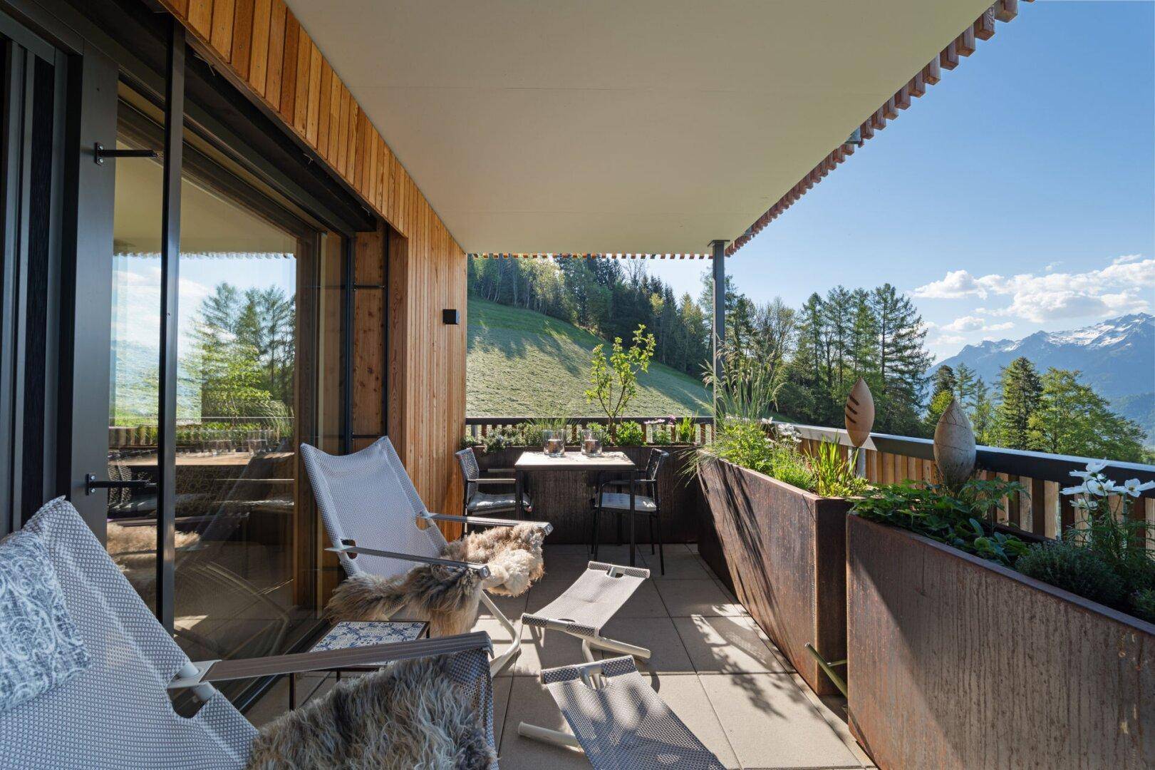 Geräumiger Balkon mit Sitzgelegenheiten, Pflanzen und Panoramablick auf die Berge und grüne Hänge.