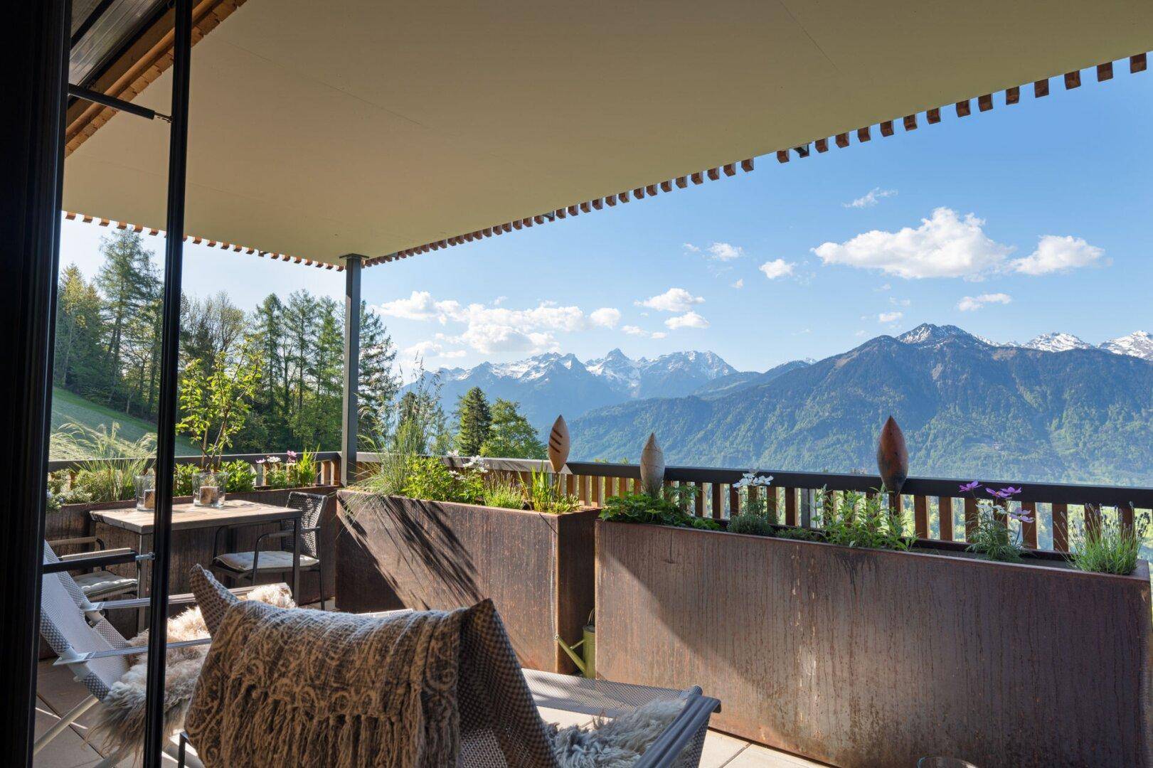 Großer Balkon mit bequemen Liegen und Esstisch, bietet einen weiten Blick auf die Alpen.
