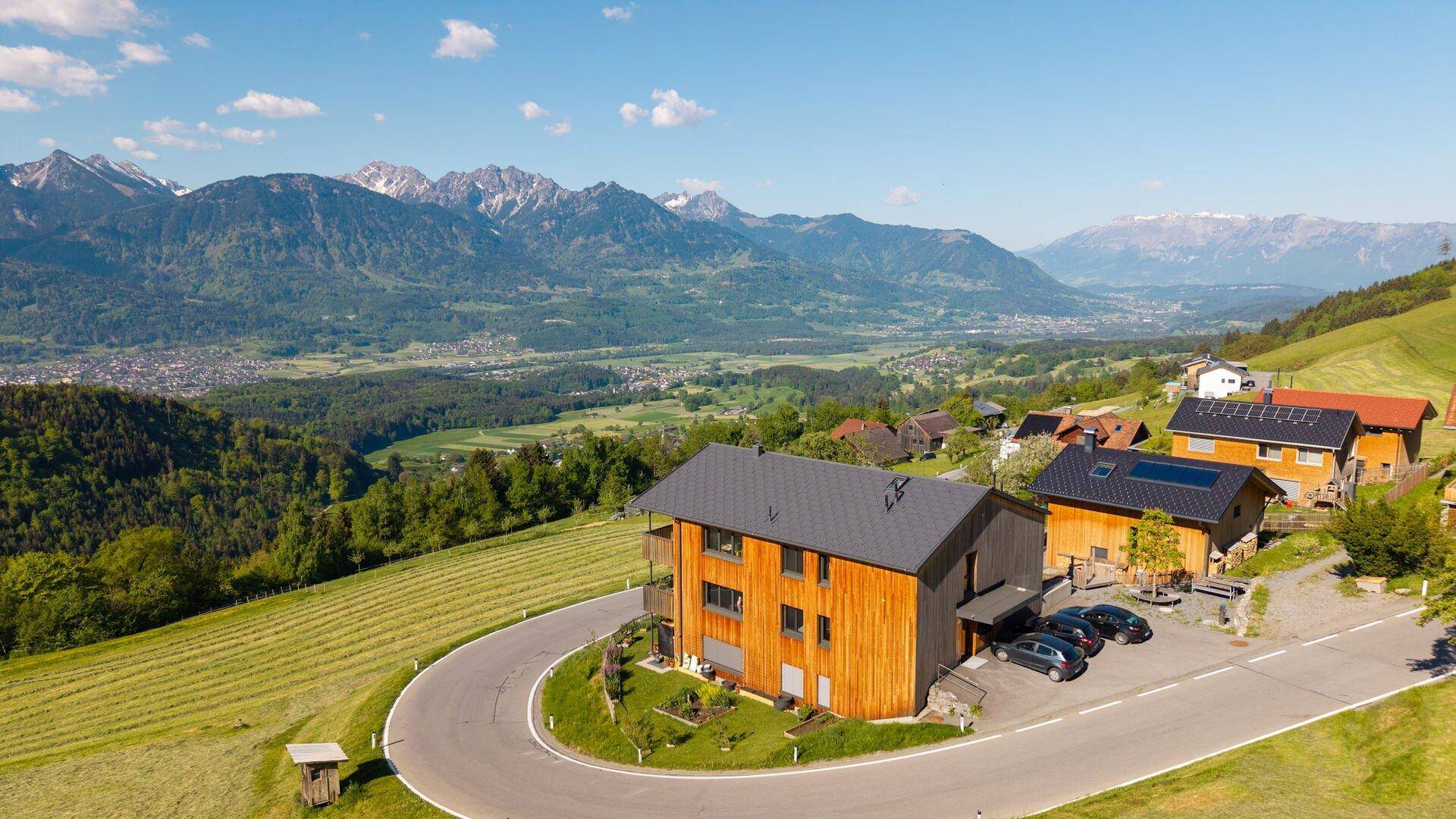 Modernes Holzhaus an einem Hang mit kurviger Zufahrt und beeindruckendem Bergblick.