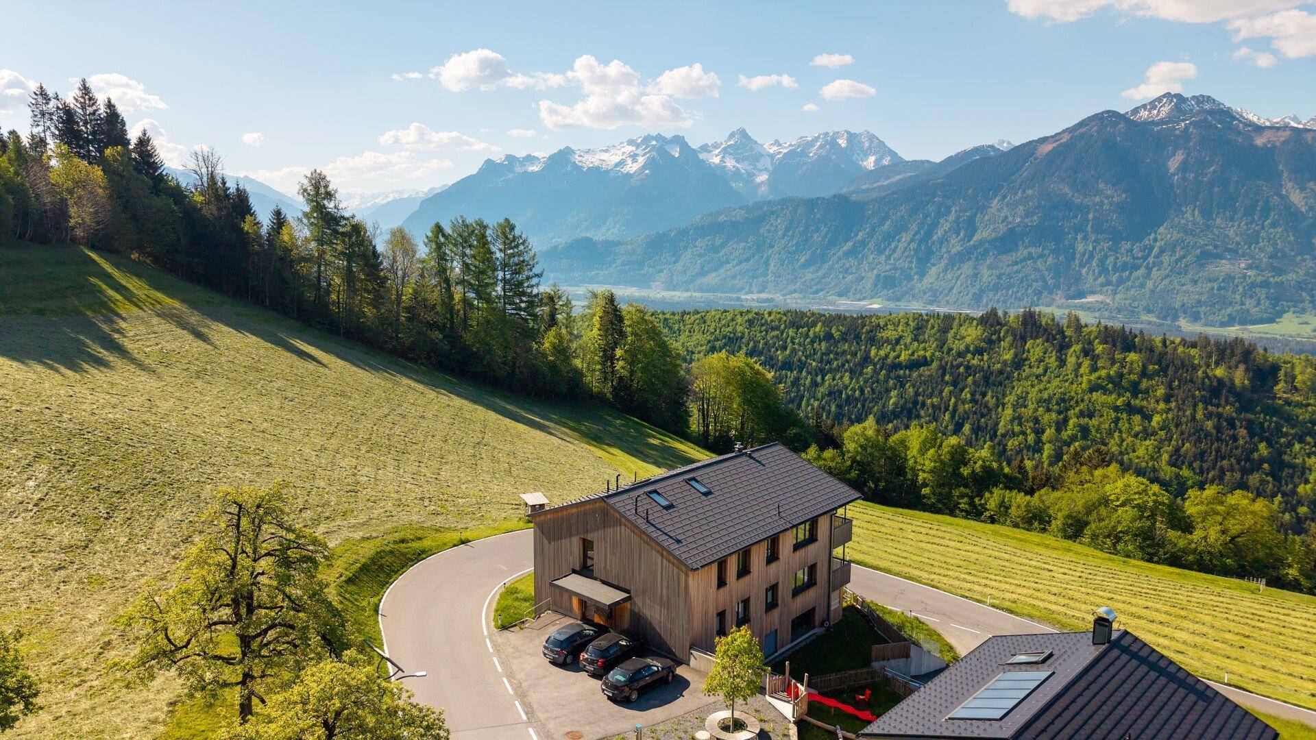 Neubau in Holzbauweise an einem Hang, umgeben von Natur und mit Bergblick.