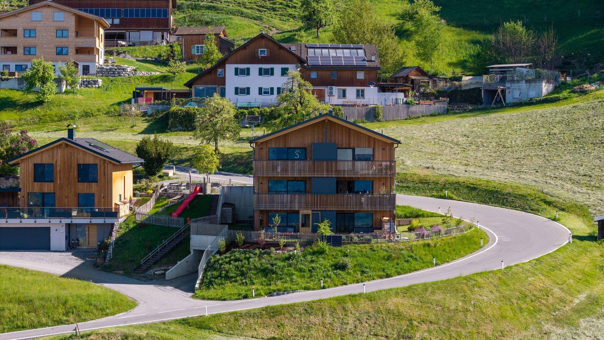Mehrfamilienhaus in Holzbauweise mit Balkonen, eingebettet in die grüne Hügellandschaft.