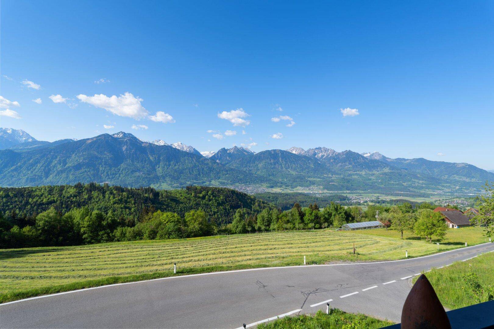 Panoramablick auf die majestätischen Berge und die weite grüne Landschaft unter einem strahlend blauen Himmel.