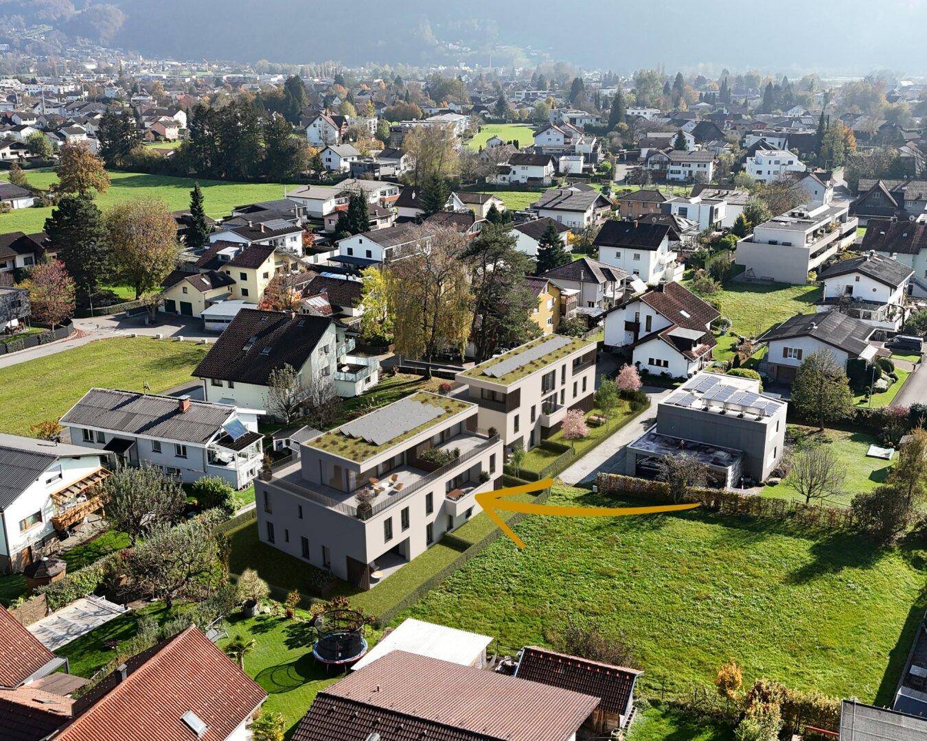 Luftaufnahme eines Neubauprojekts in einer grünen Wohngegend mit umliegenden Häusern und Bergblick.