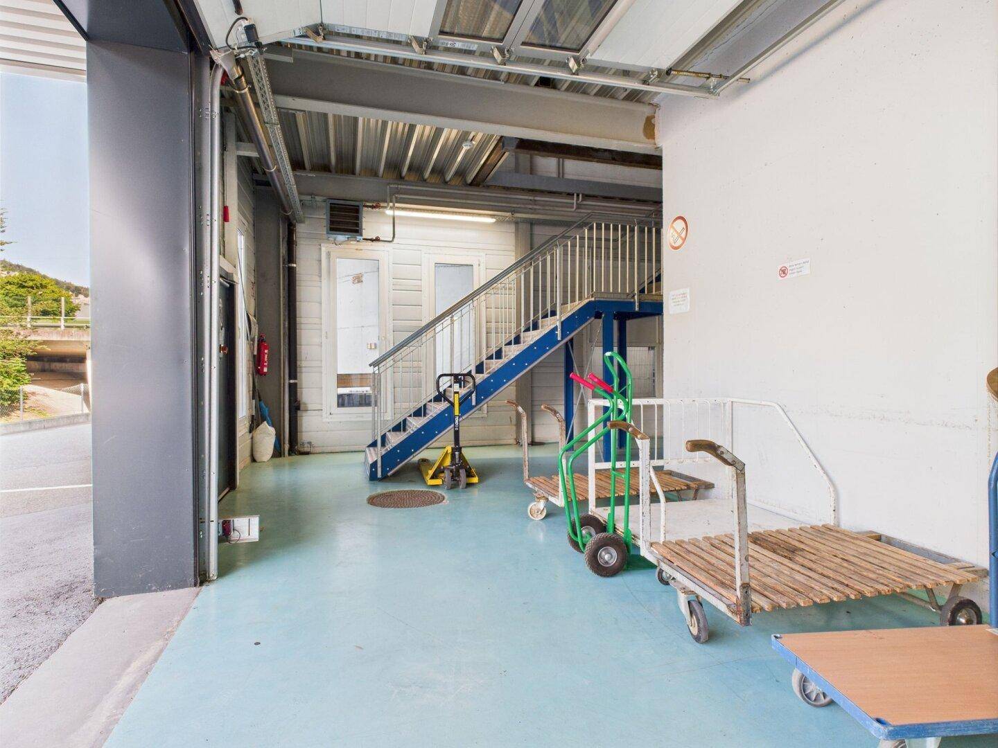 Ladebereich mit blauer Stahltreppe und verschiedenen Transportwagen, bereit für den Warenverkehr.