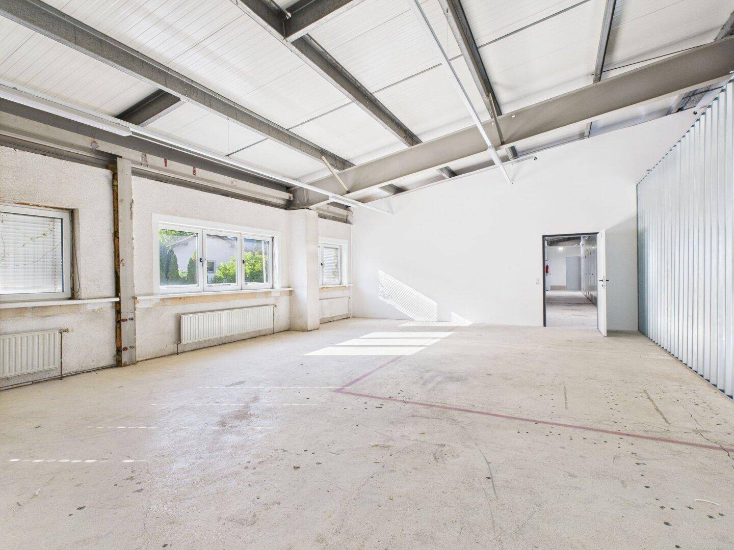 Großer, leerer Gewerberaum mit Betonboden, weißen Wänden und sichtbaren Deckenbalken aus Metall.