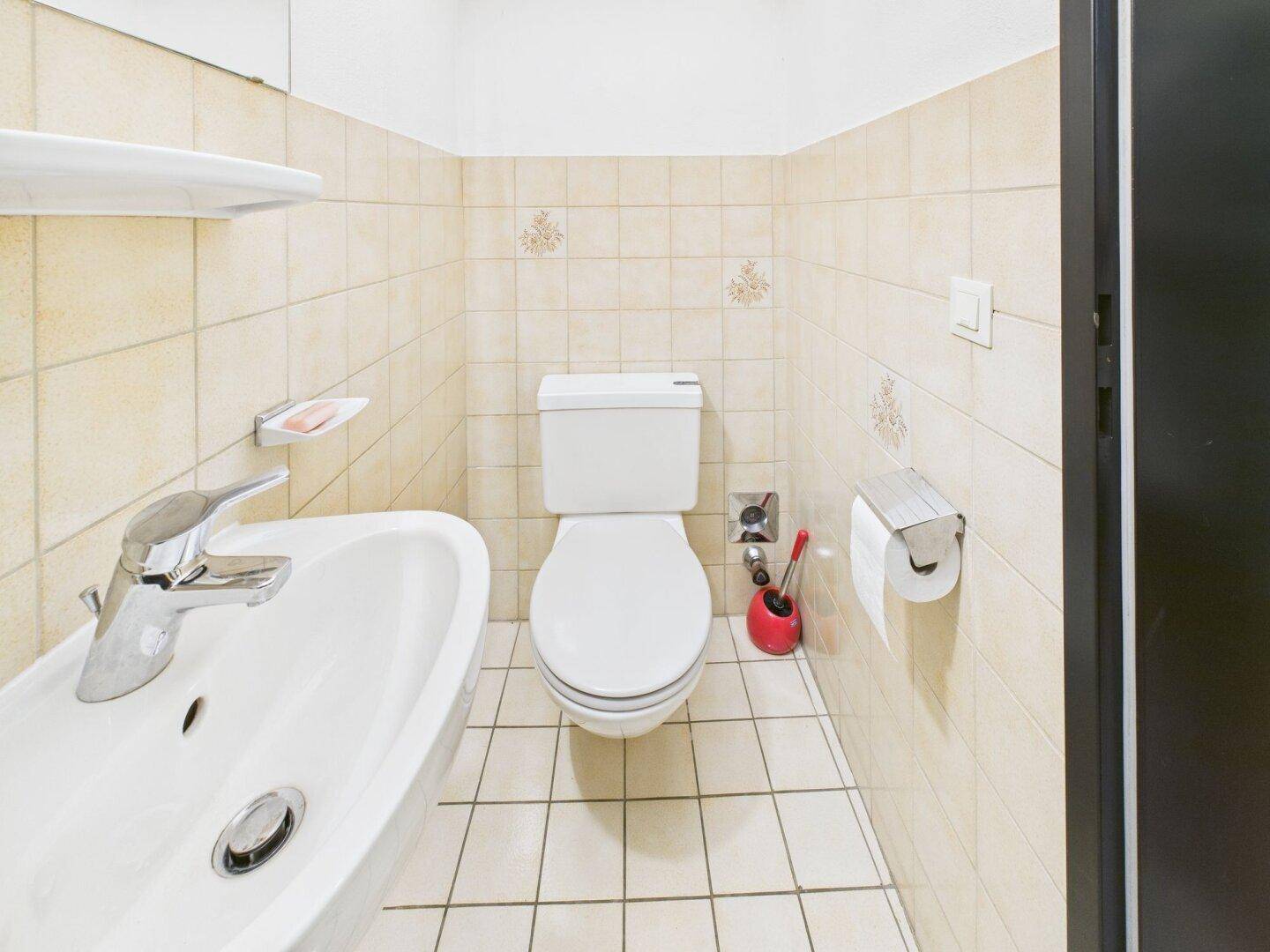 Gästetoilette mit beigefarbenen Fliesen, WC und Waschbecken.