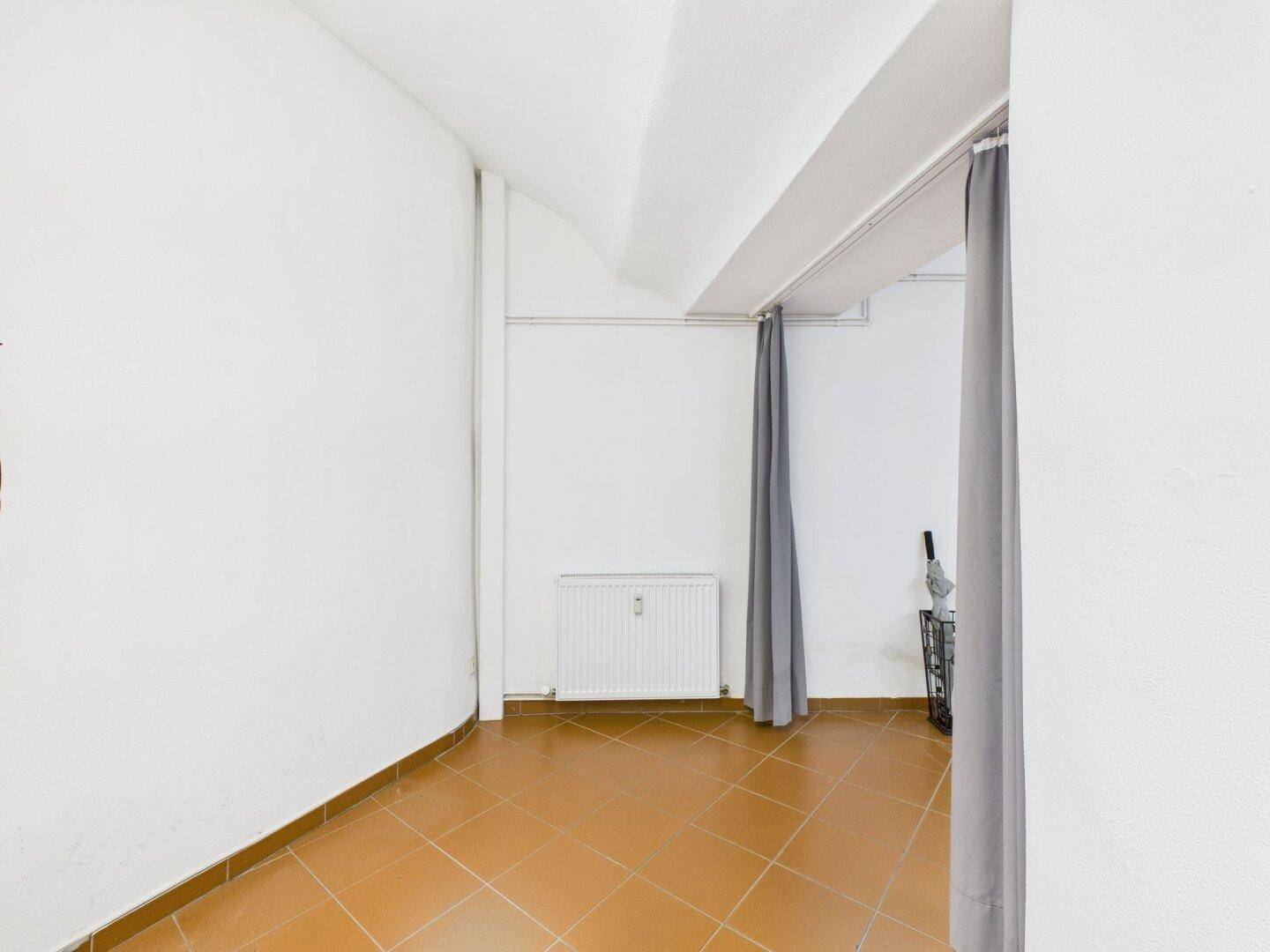 Kleiner Raum mit gewölbter Decke, Terrakottafliesen und Heizkörper, abgetrennt durch einen Vorhang.