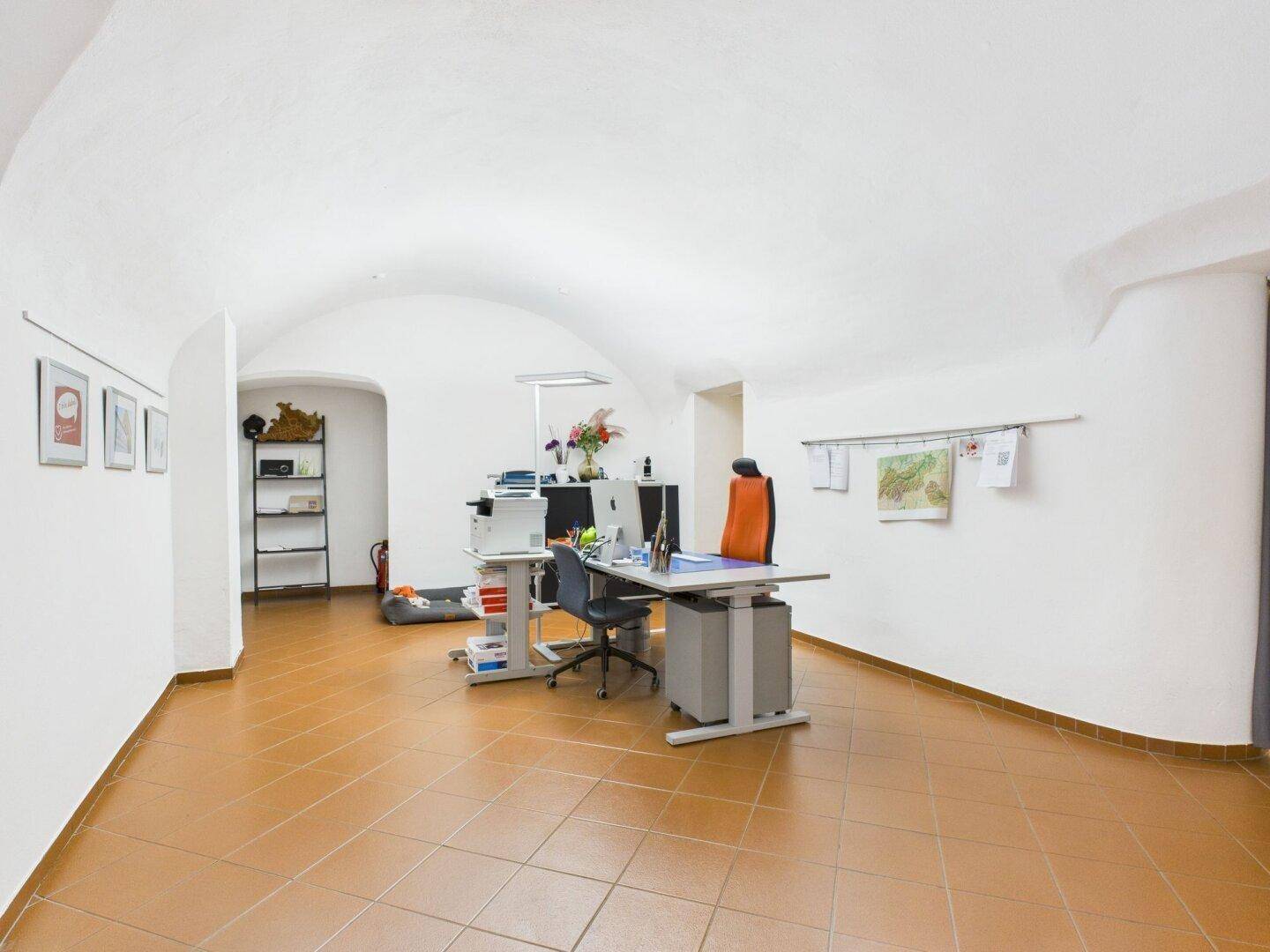 Weitläufiges Büro mit gewölbter Decke, Terrakottafliesen und mehreren Arbeitsplätzen.