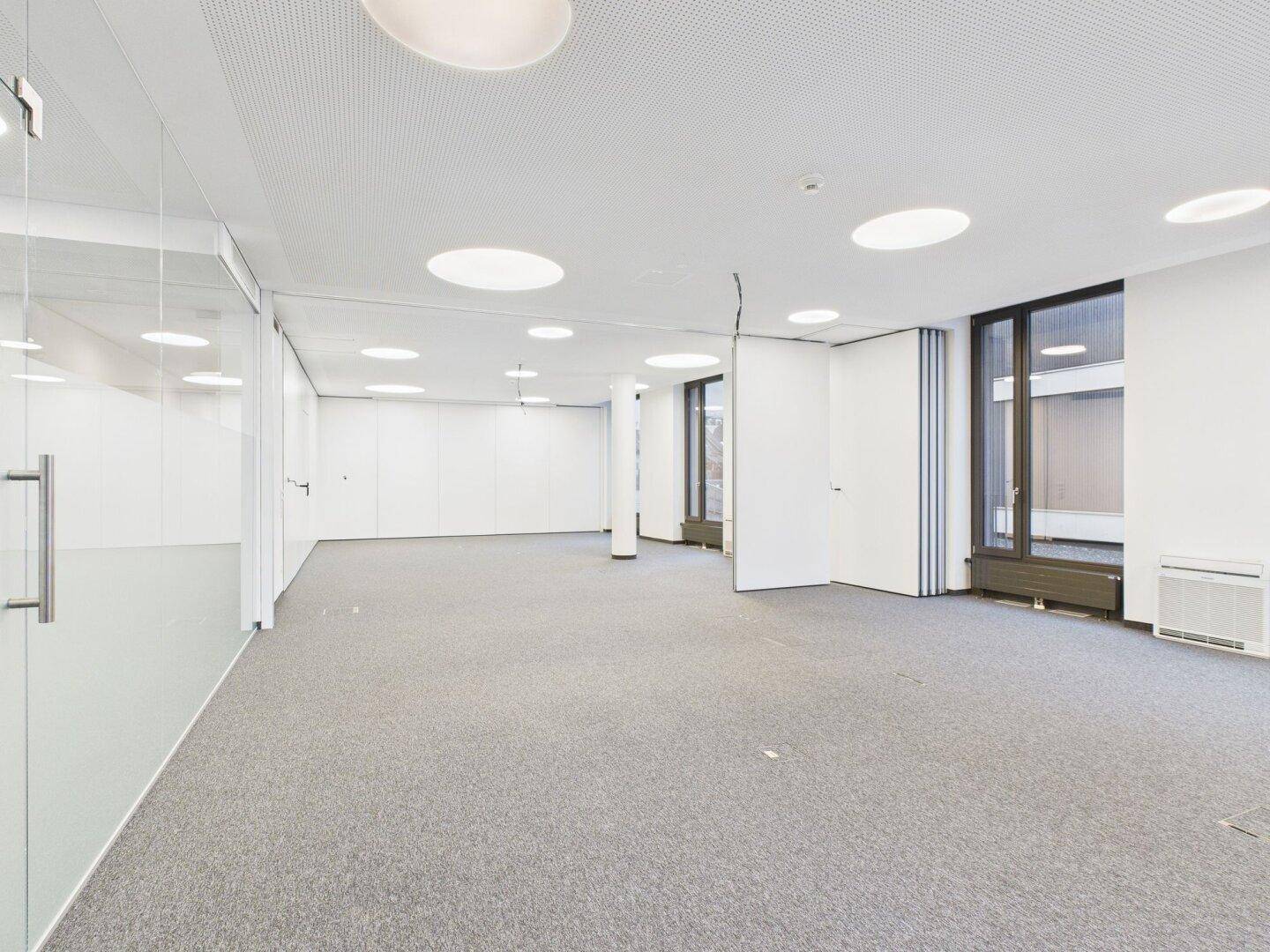 Geräumiger Bürobereich mit Teppichboden, Glaswänden und großen Fenstern für helle Arbeitsplätze.