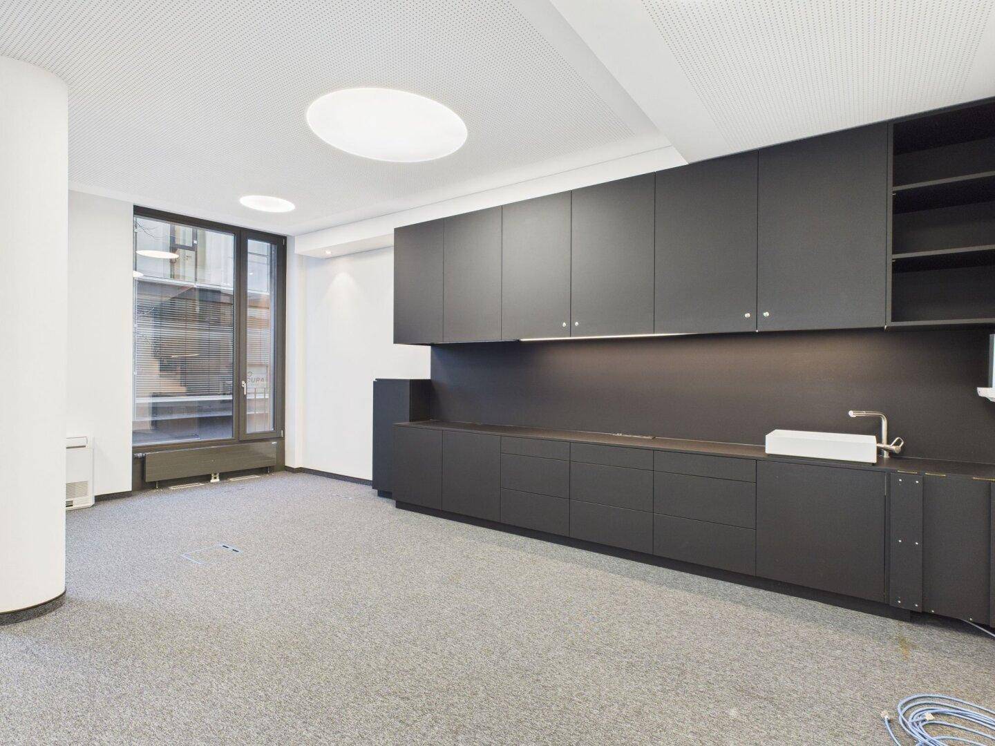 Moderne Küchenzeile in dunklem Grau mit Spüle, viel Stauraum und integrierter Beleuchtung.